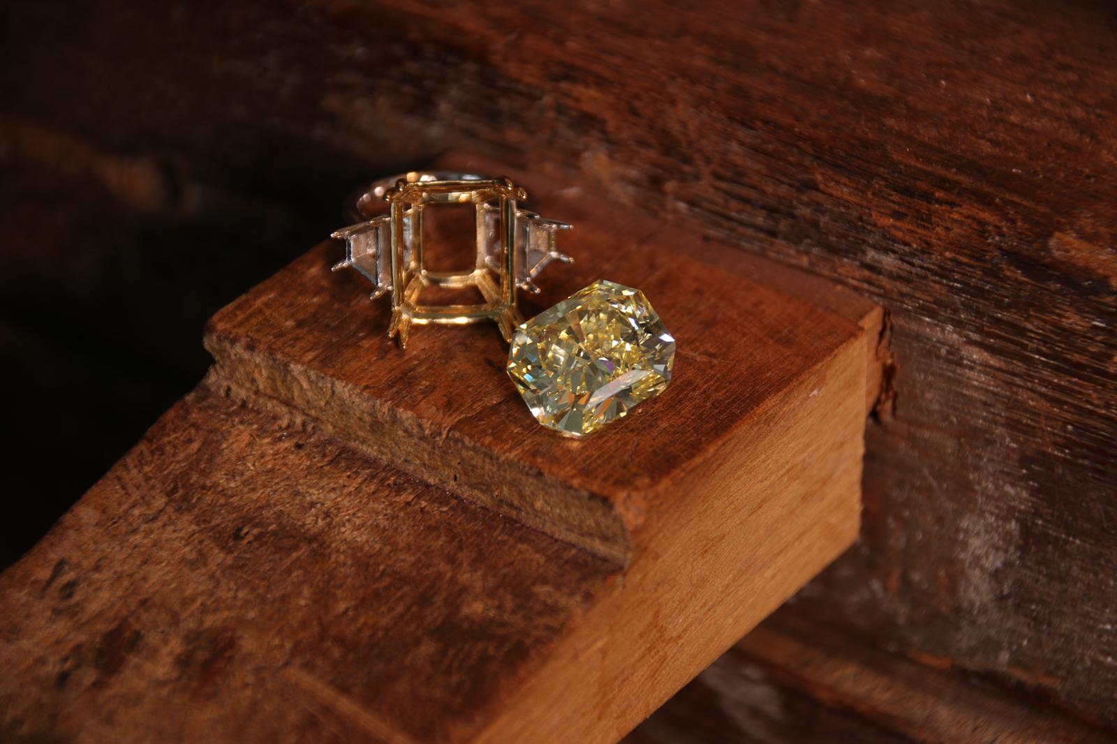 Fancy yellow radiant-cut diamond beside its setting on wood